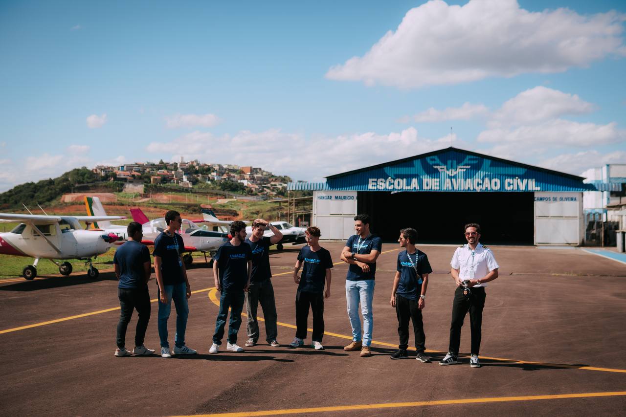 Alunos conversando no pátio com aeronaves e o hangar ao fundo